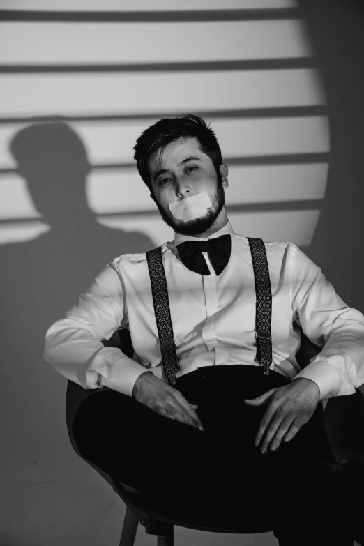 black and white po of a man wearing suspenders sitting on a chair