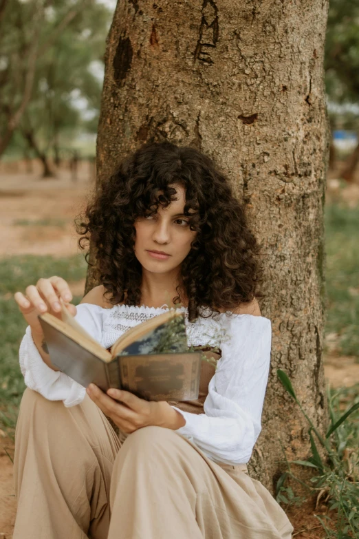 a woman with curly hair sitting on the ground holding an open book