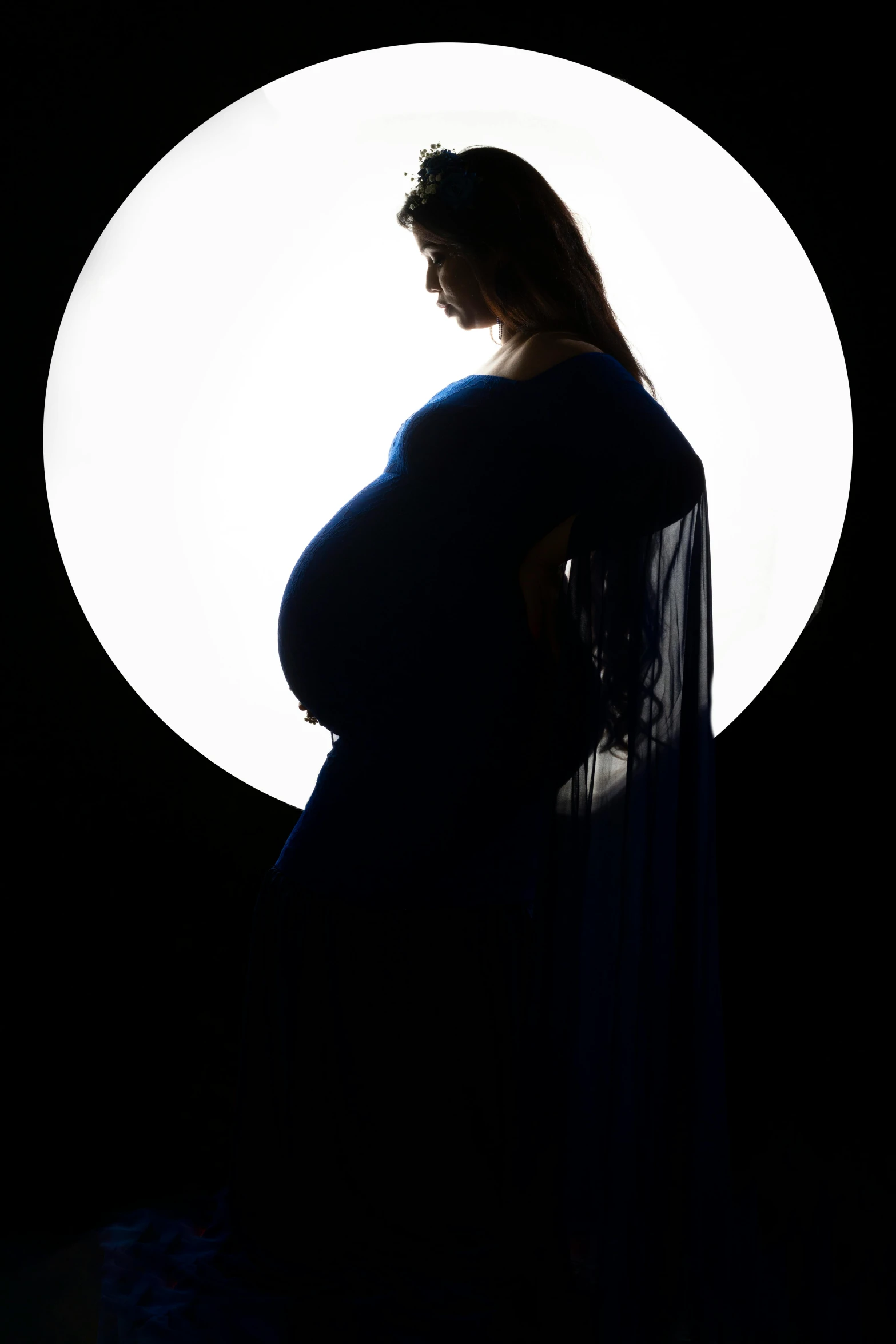 a pregnant woman looking down at her belly in the dark