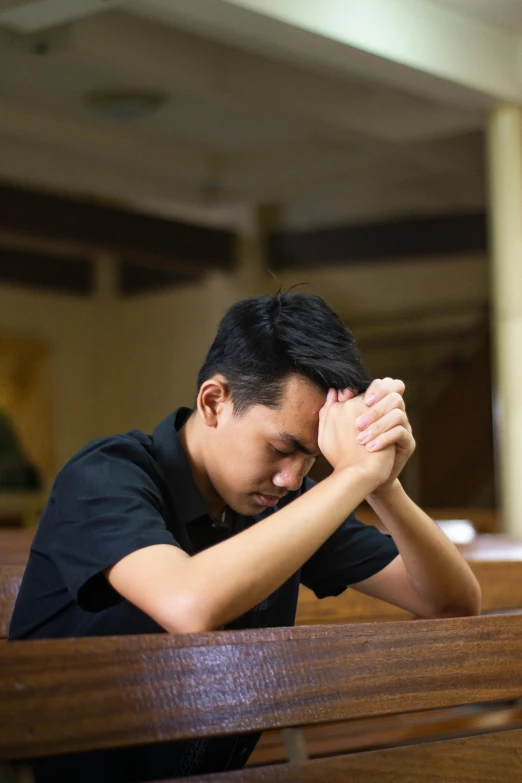 a man with his hands together sitting in a pew