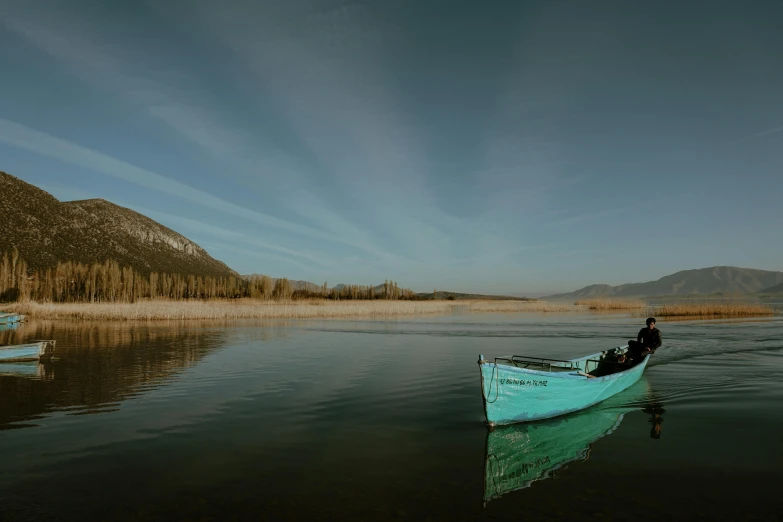 a man is riding in a blue rowboat on a calm river