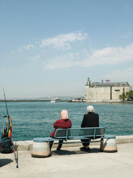 two women sit on a bench overlooking the water and city