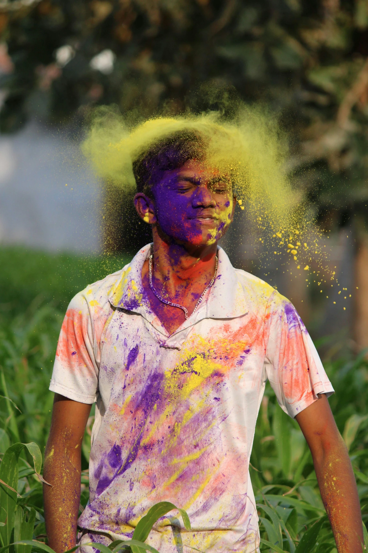a man covered in yellow and purple powder standing next to a cornfield
