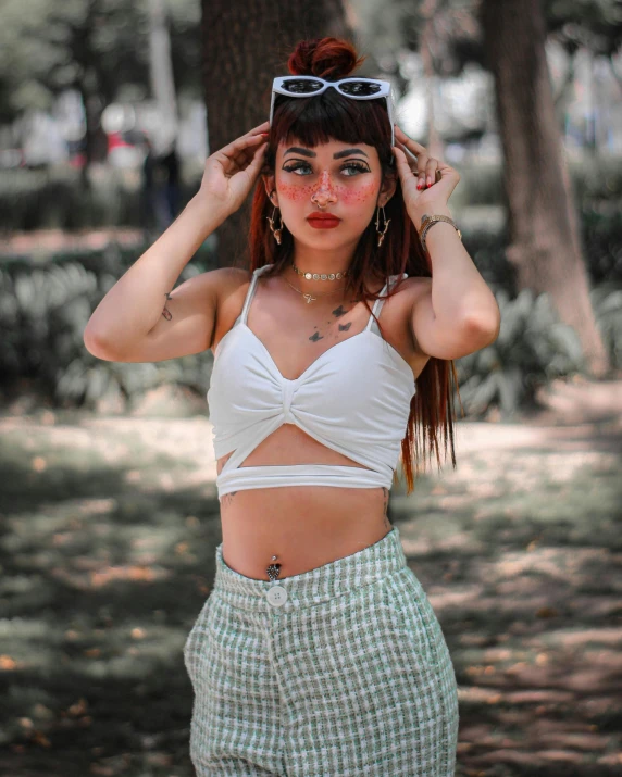 a woman wearing a crop top and high waist skirt with a hair bun and round sunglasses