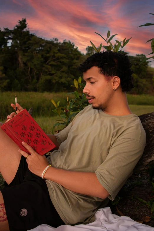 a man in grey shirt holding a book near trees