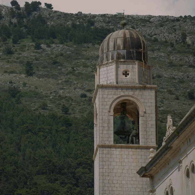 a bell tower stands in front of a hillside