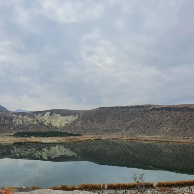 a small pond surrounded by mountains under a cloudy sky