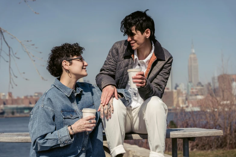 two people sitting on a bench talking over a drink