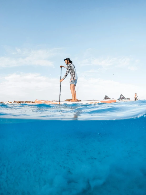 woman standing on a surfboard on the surface of water with a sky background