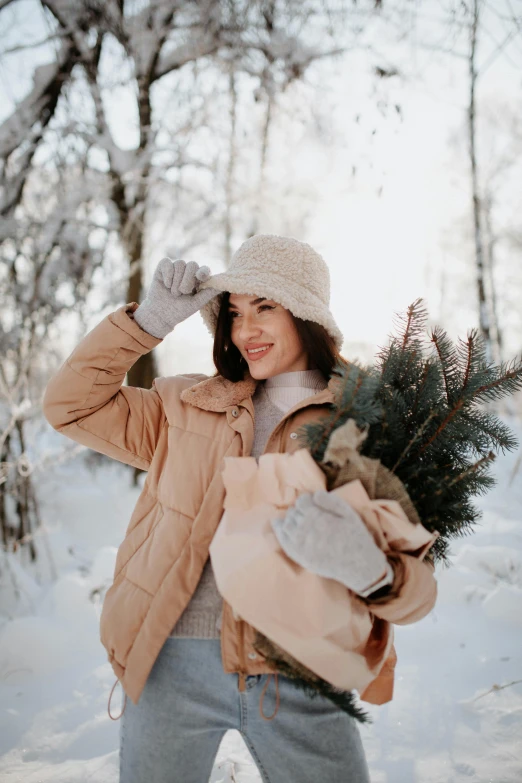 a woman in winter clothes is holding a pine tree