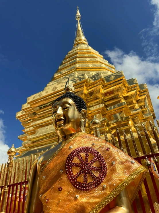 a statue of a gold buddhist monk in front of a golden building