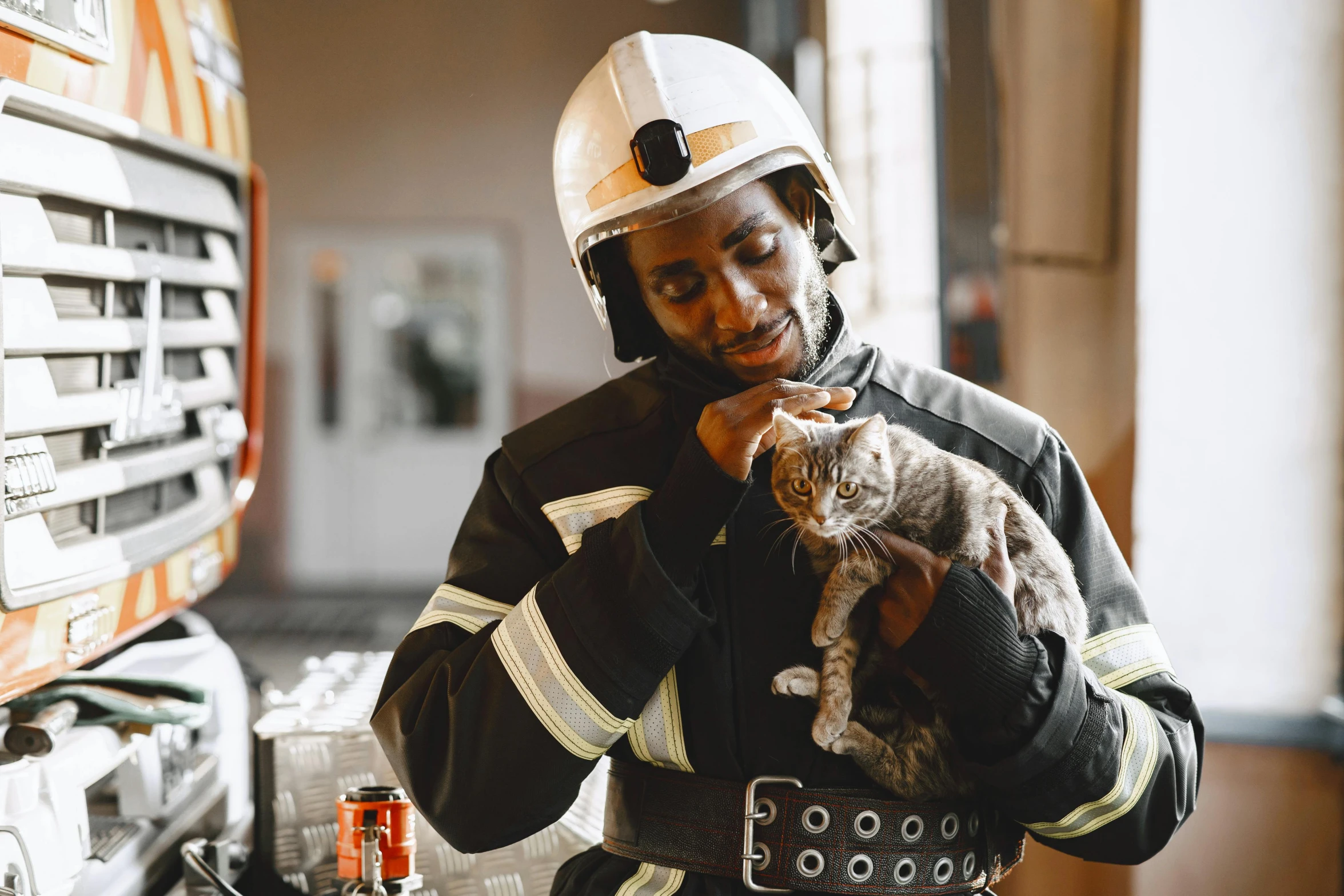 a man in safety gear holding a cat near fire station