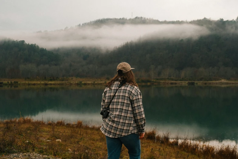 person with long hair stands on rock looking out over a lake