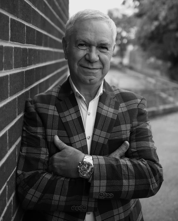 the man in a plaid jacket stands near a brick wall