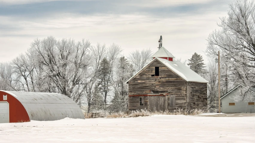 an old barn is standing near another house with snowy trees around it