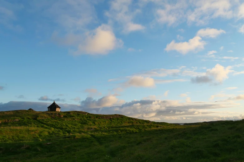 the green hillside is covered in clouds and an unusual house