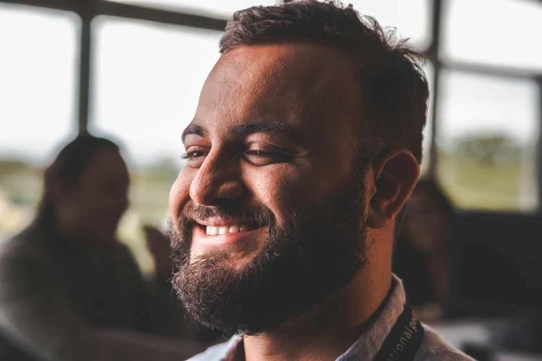 a bearded man smiling by a window in a sunny room