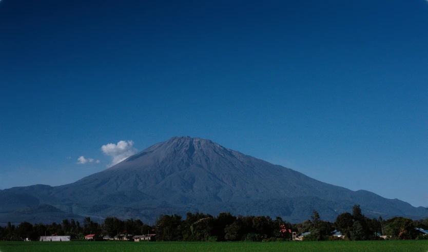 a view of a volcano towering over a green field