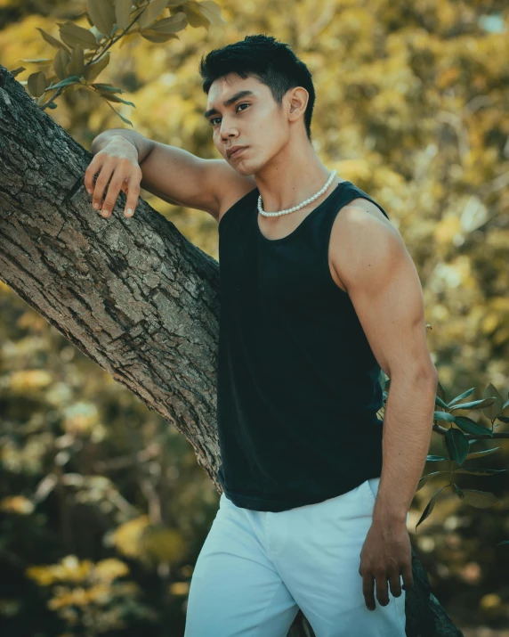 a man in a tank top is leaning against a tree