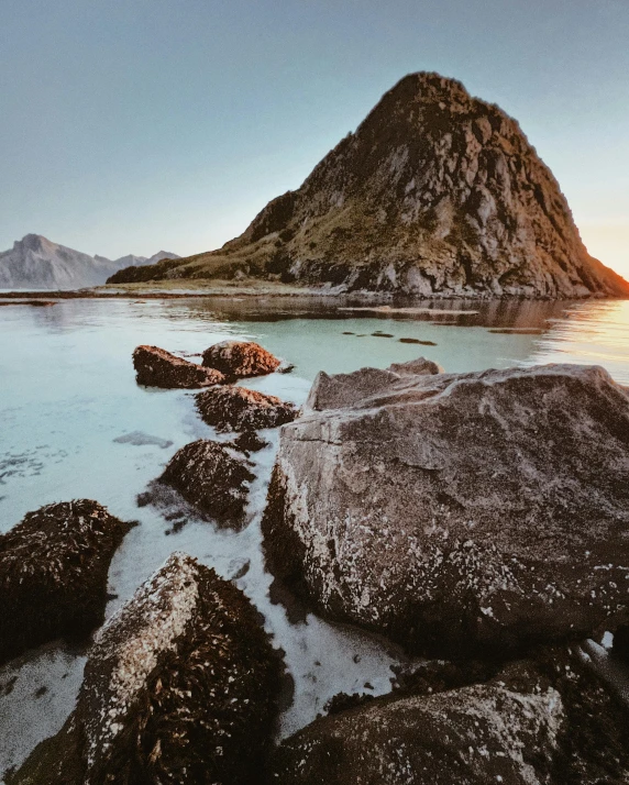 a large mountain is in the background with rocks on the ocean