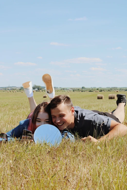 a young couple lays in a field and cuddles with frisbees