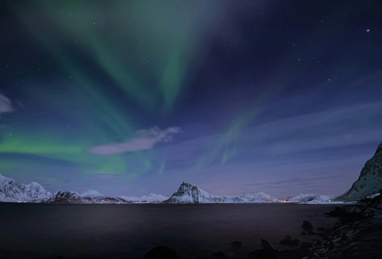 a green and purple aurora bore in the night sky over water