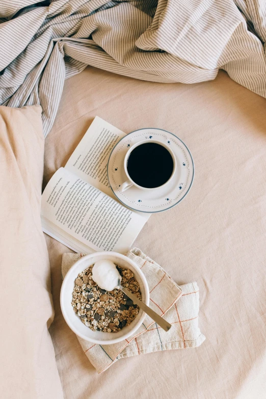 a cup of coffee and an open book sitting on a bed