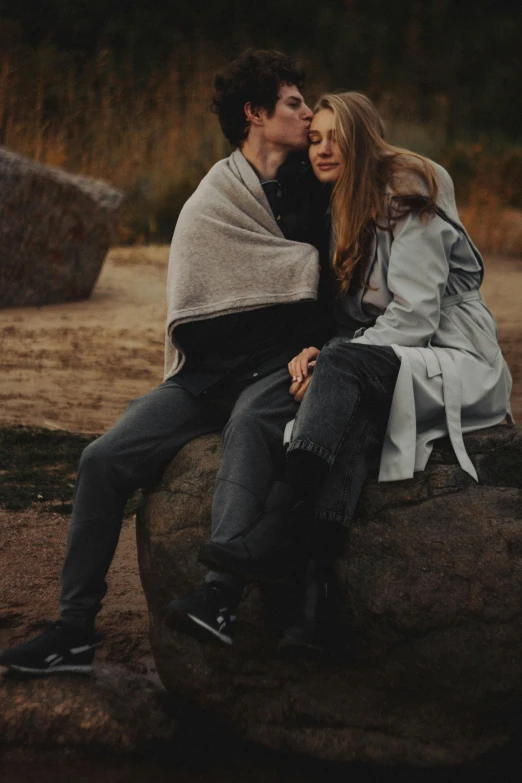 a man and woman sitting on a rock and kissing