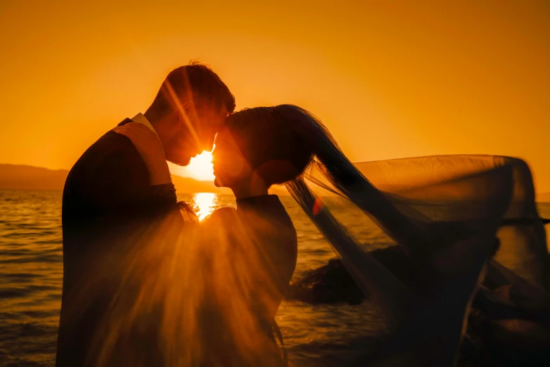 a couple is kissing with the sun setting in the background