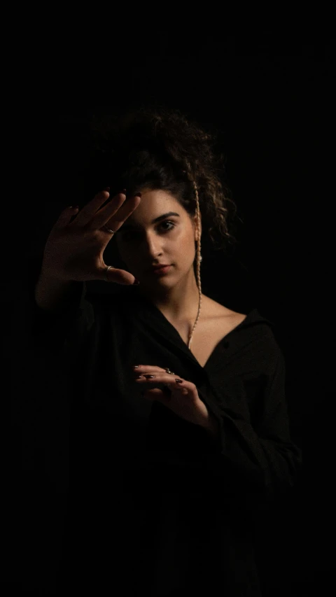 an african american woman with curly hair wearing a black top, standing and posing with her hand in the air