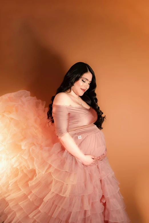 pregnant woman in light pink dress leaning on a tan wall