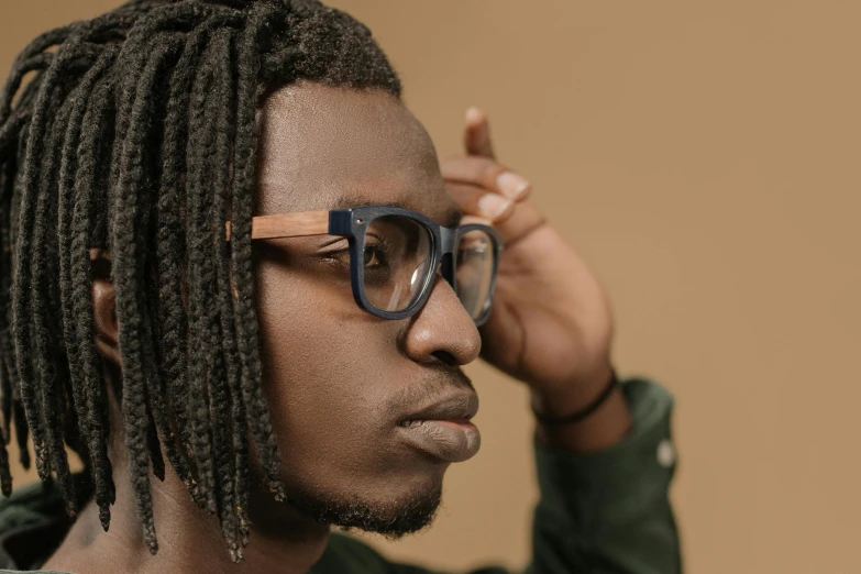 a man with glasses on, with dreadlocks holding his ear