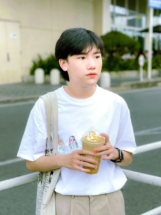 a young man with a cup of coffee stands in front of a white fence