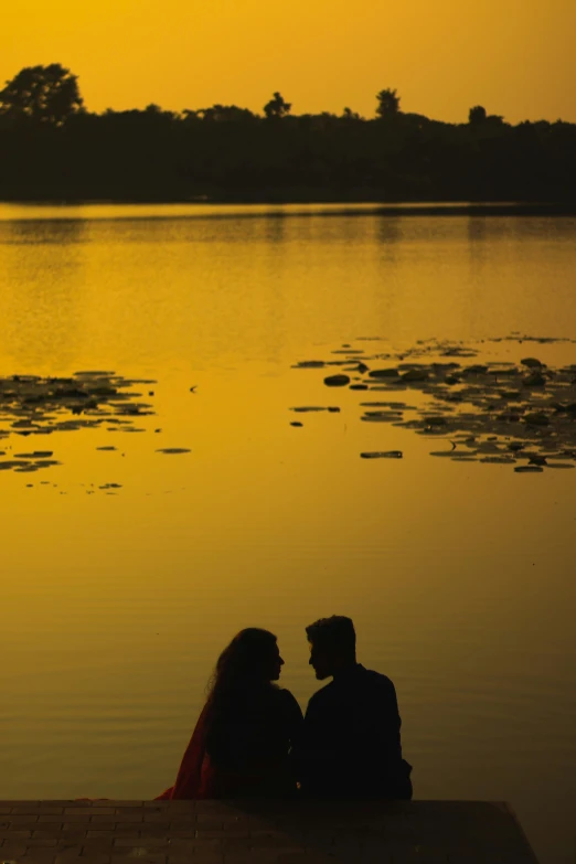 two people are sitting on a bench in front of a body of water