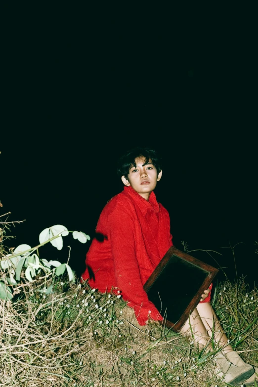 an old woman sitting in the grass holding a piece of luggage