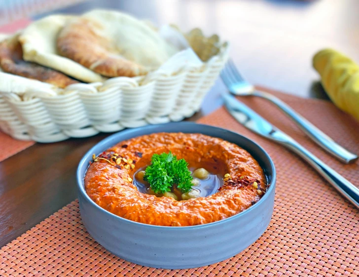 an orange, yellow, and white dish is on a table with a basket of silverware