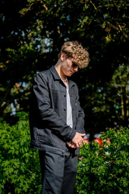 a man looks down while leaning against a tree