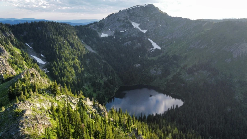 a large crater surrounded by forested trees in a mountain area