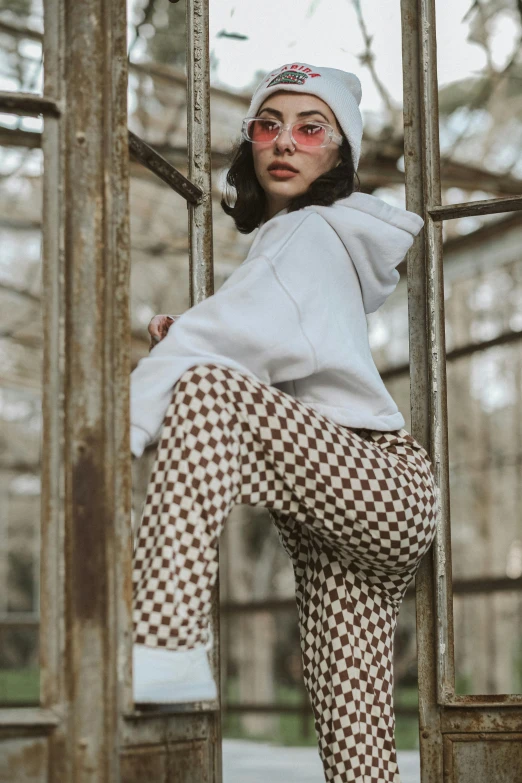 woman wearing glasses and patterned pants posing by some rusted metal