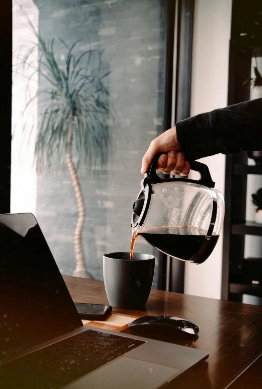 a person pours coffee into their coffee cup on top of a desk