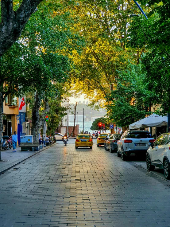 a yellow car parked in front of trees and people walking on a sidewalk