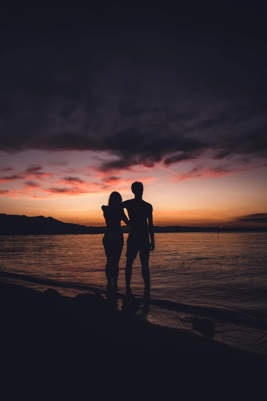 a couple is standing on the beach at sunset