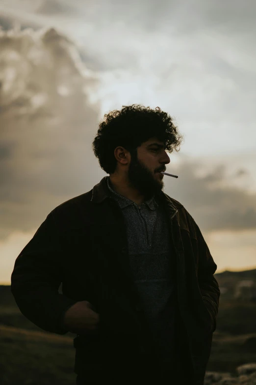 a man with a beard standing and smoking a cigarette