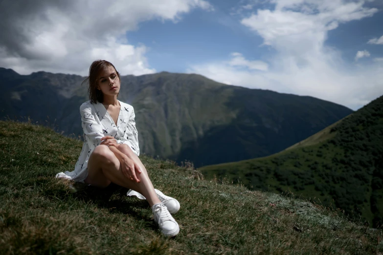 a young woman is sitting in the grass on the edge of a mountain