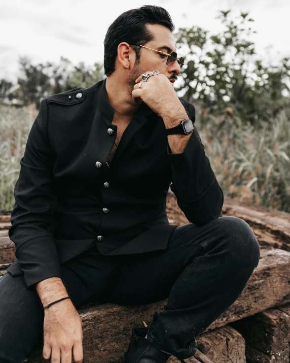 a man sits on a tree stump wearing a suit and watch