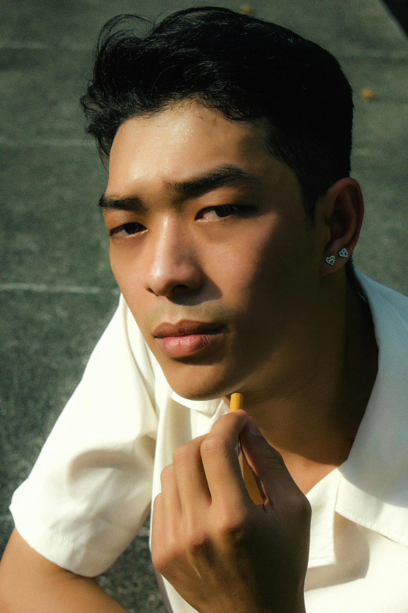 a young man sitting in the shade with his hand on his nose