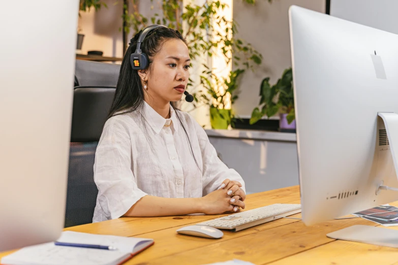 woman wearing headset at desk in office with monitor and laptop