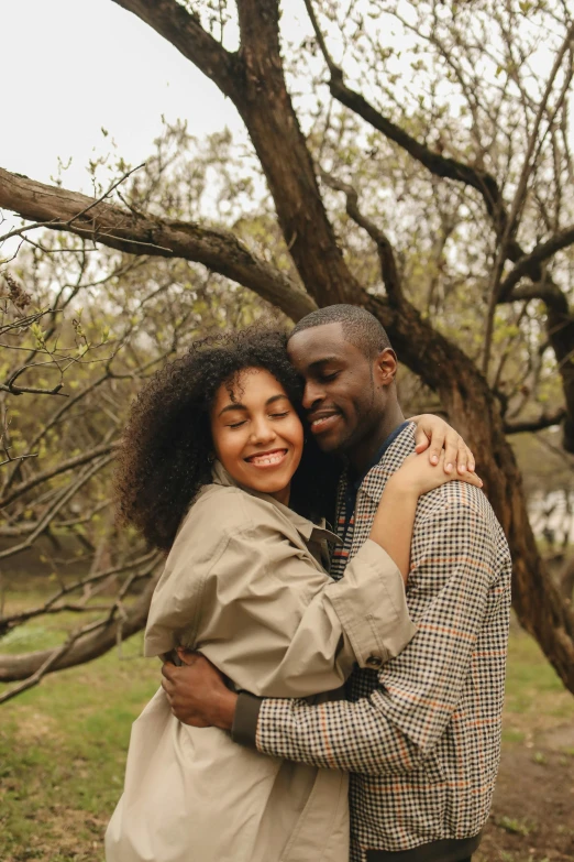 a black man and black woman hugging each other in front of a tree