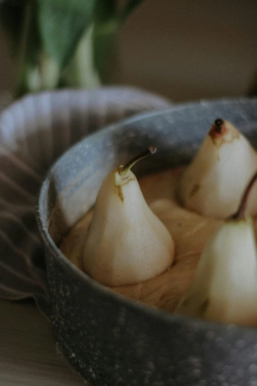 pears are in a metal bowl next to a leaf