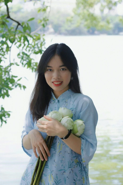 a woman holding flowers standing in front of a lake